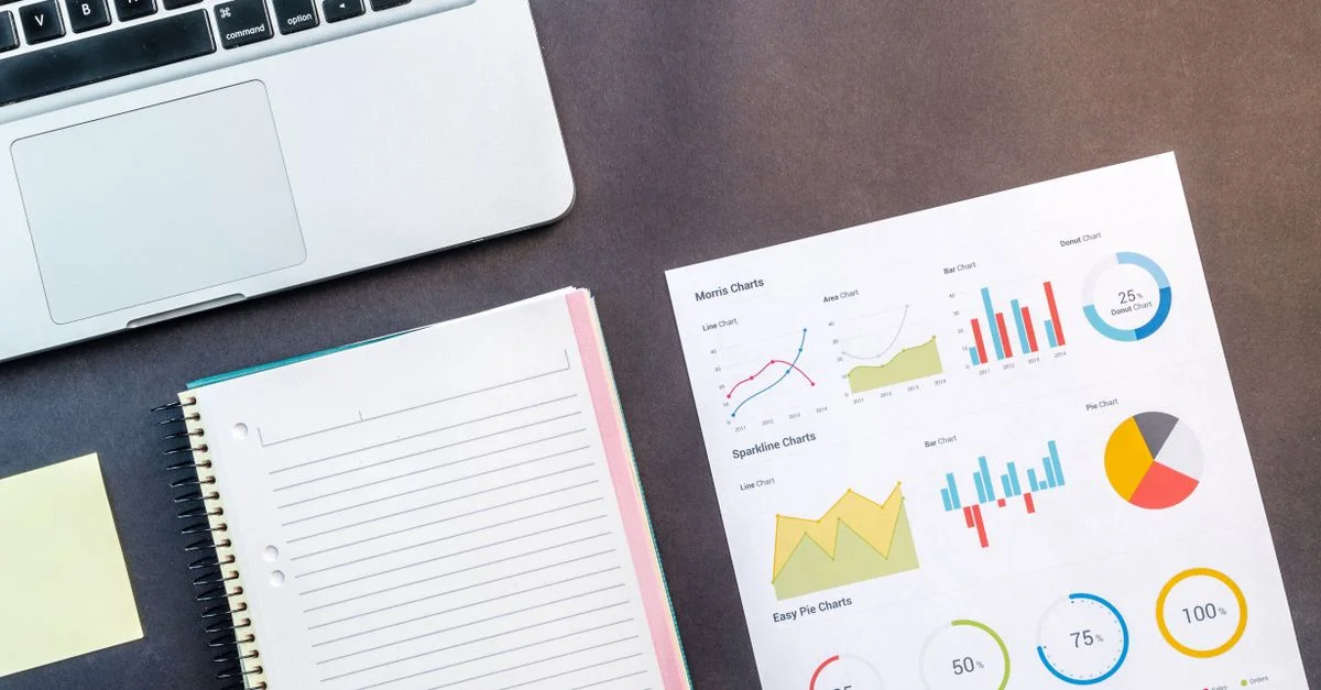 Vue de dessus d'un ordinateur portable, d'un carnet et de graphiques de données sur une table, idéal pour des thèmes d'affaires et de travail.
