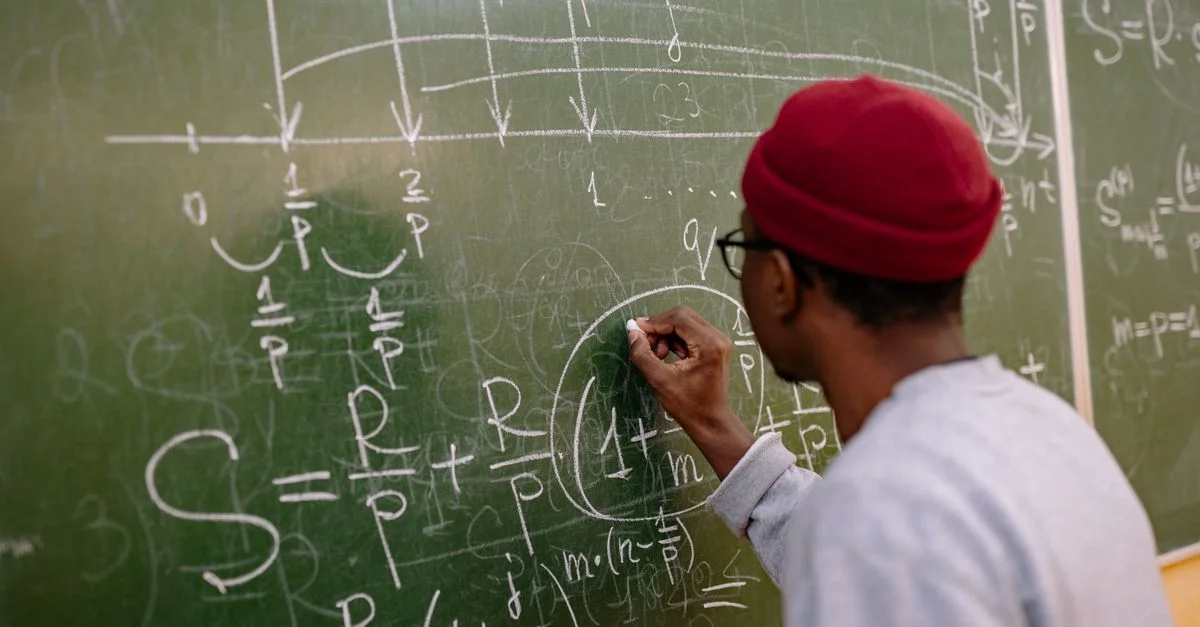 Étudiant écrivant des équations mathématiques complexes sur un tableau dans une salle de classe.