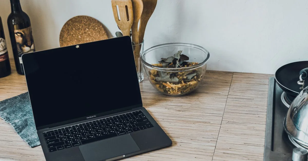 Plan de travail de cuisine élégant avec un ordinateur portable, des ustensiles, une bouteille de vin et un équipement de cuisine.