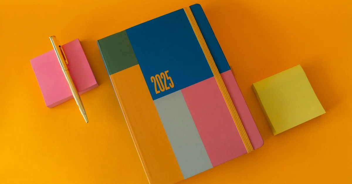 Agenda 2025 dynamique et arrangement de stylos avec des notes autocollantes colorées sur une surface orange.