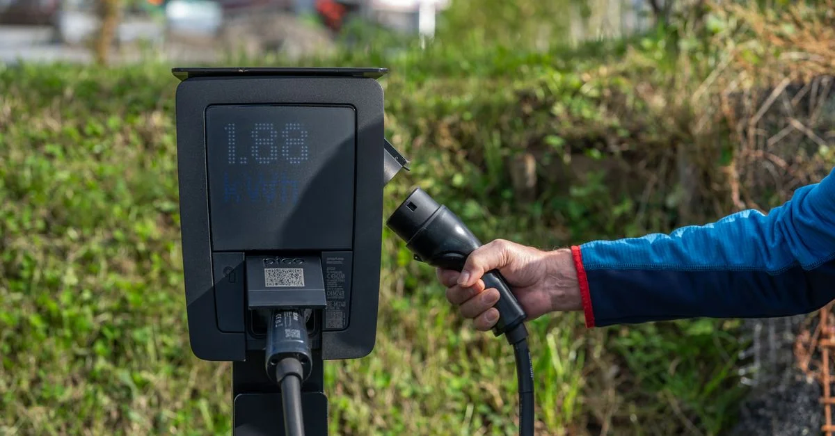 Une station de recharge électrique en extérieur avec une main tenant un câble de recharge.